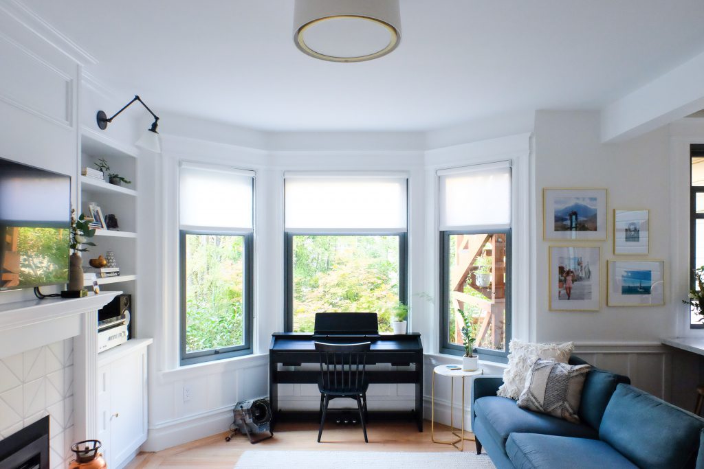 a piano sits in front of brightly lit bay windows.