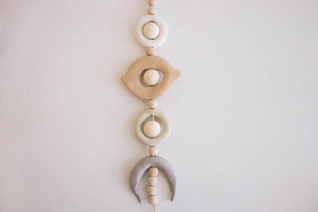 Continue in this manner, placing a half-inch wooden bead in between the clay beads and a one-inch wooden bead inside them, starting with the eye shape, another full moon shape, and then the crescent moon shape. Thread four wooden beads onto the cord after the crescent moon.