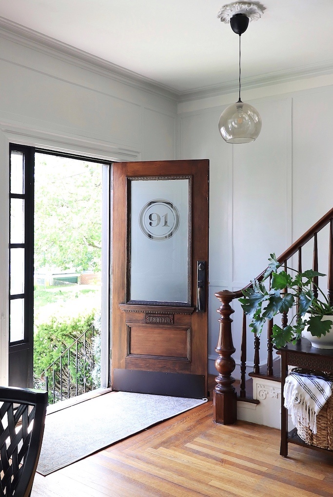 The renovated entryway has a clear glass globe pedant light and a dark wood door
