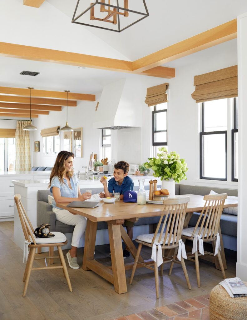a dining table with rosa and her child sitting at it. one side of the table has wooden chairs and the other side has a small gray sofa.