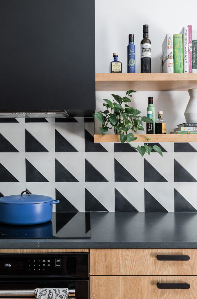 a close up of the oven with a blue Dutch oven on the range, open shelving with bottles and a plant, and the countertop.